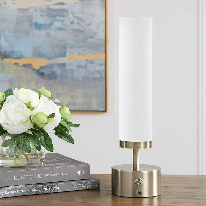 A modern table lamp with a tall white cylindrical shade and brushed brass base