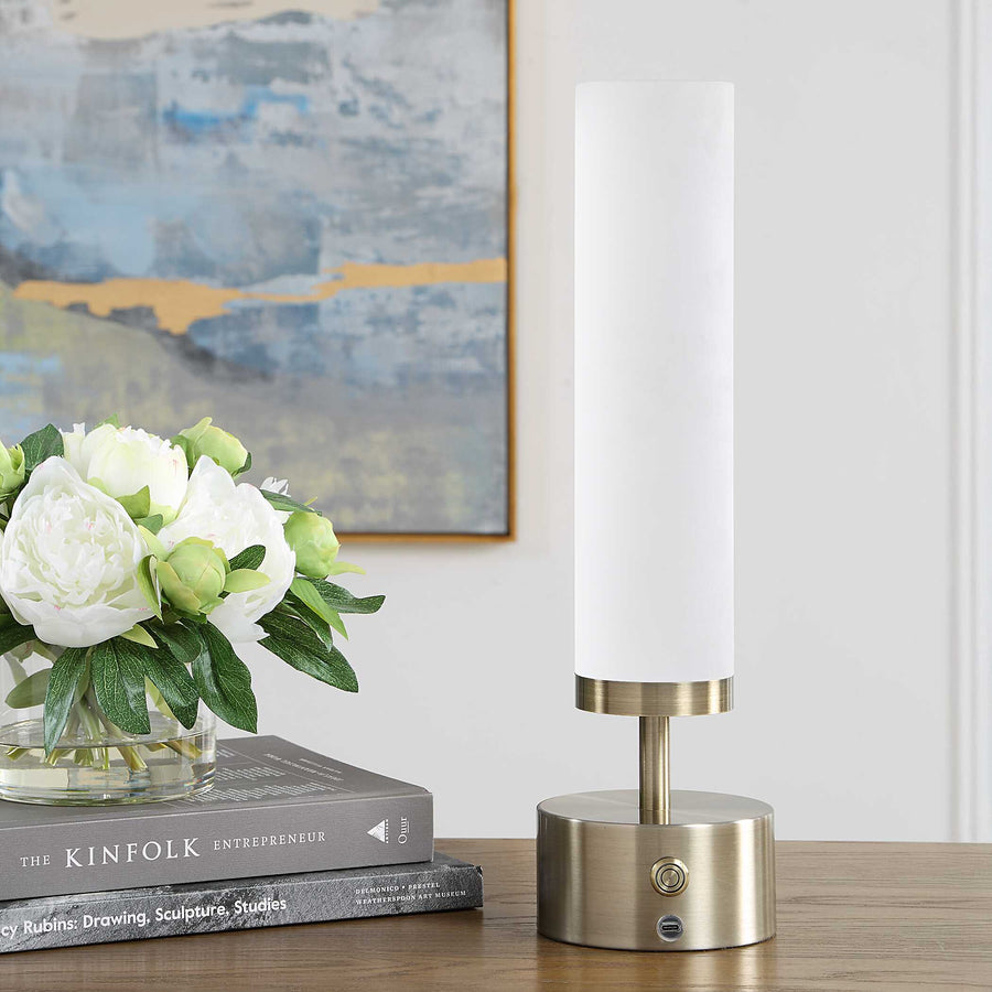 A modern table lamp with a tall white cylindrical shade and brushed brass base