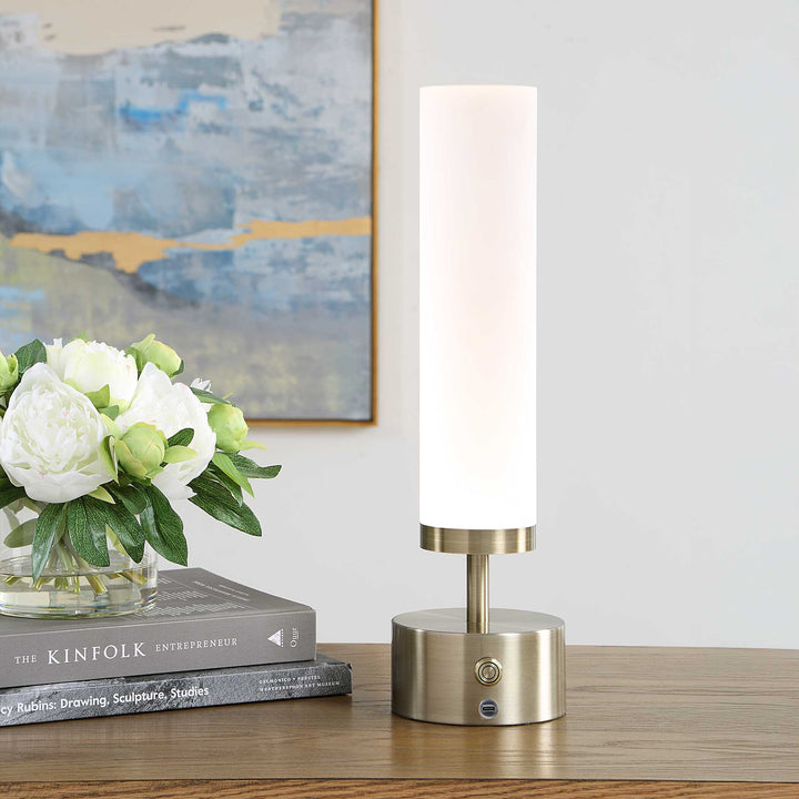 A modern table lamp with a tall white cylindrical shade and brushed brass base
