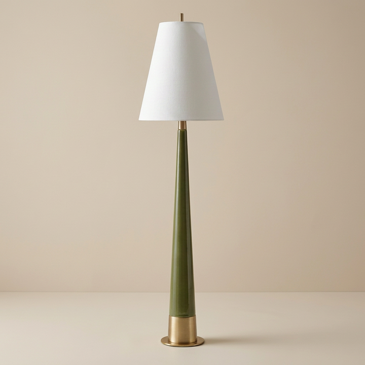 mid-century modern style table lamp with a tall, slender tapered ceramic body in a glossy moss green finish. The lamp features a brushed gold metallic base and matching neck hardware, topped with a crisp white tapered fabric drum shade