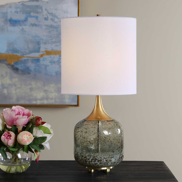 A table lamp with a white drum shade, a gold-finished neck, and a speckled glass base