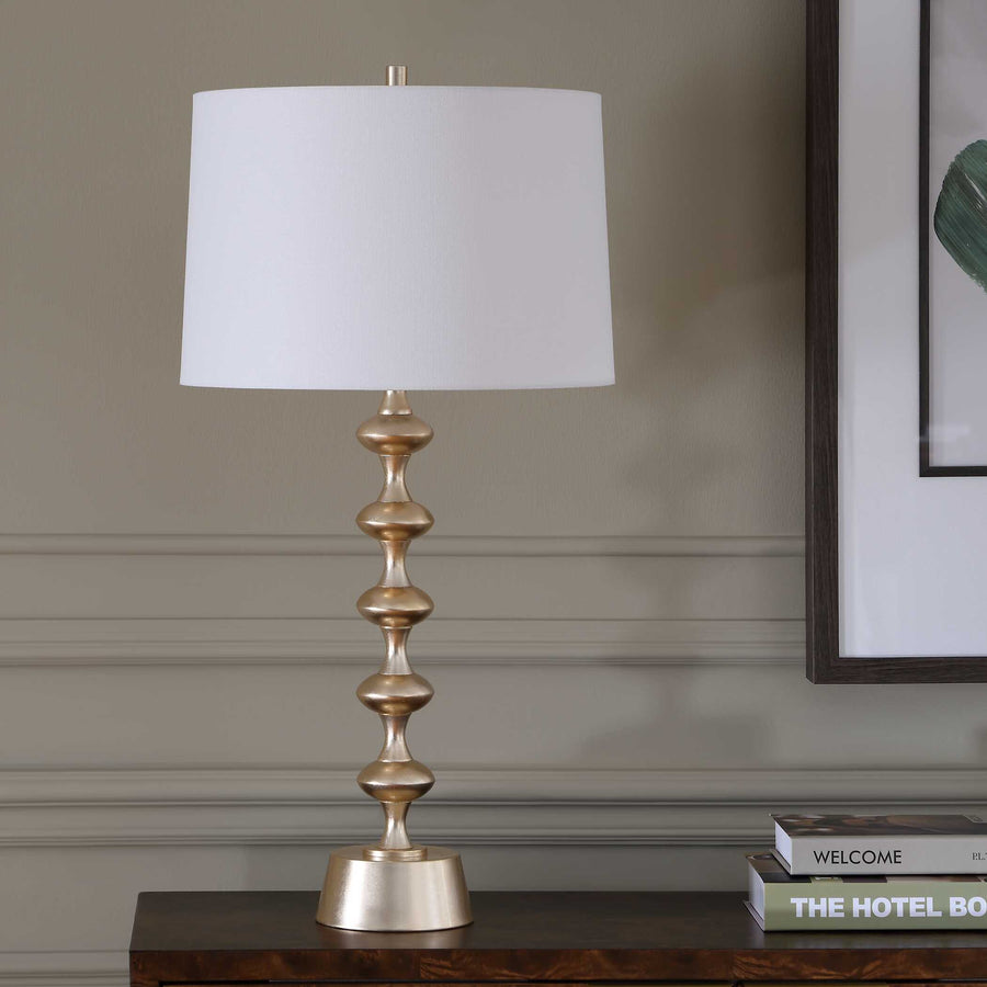 Decorative table lamp with a gold base and white shade on a wooden surface.