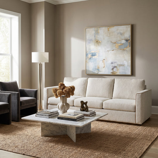 Modern living room with a cream sofa, marble coffee table, abstract art, and a jute rug in a neutral, minimalist interior.