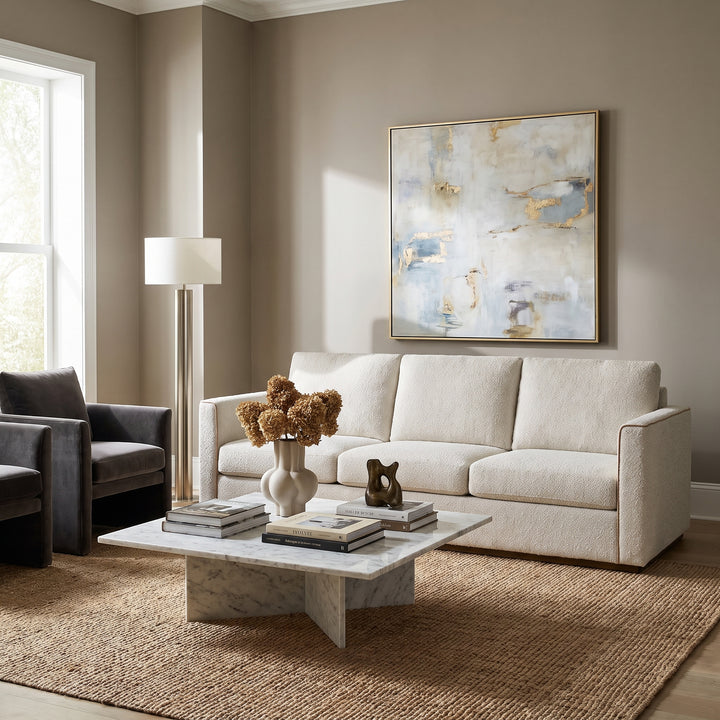 Modern living room with a cream sofa, marble coffee table, abstract art, and a jute rug in a neutral, minimalist interior.