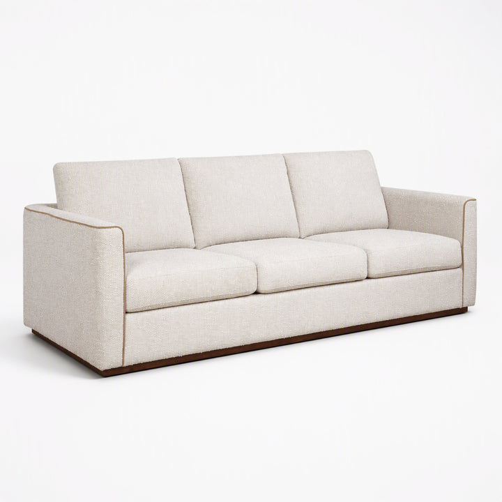 A modern three-seater sofa upholstered in a light beige textured fabric, featuring a low wooden base, shown on a seamless white background.