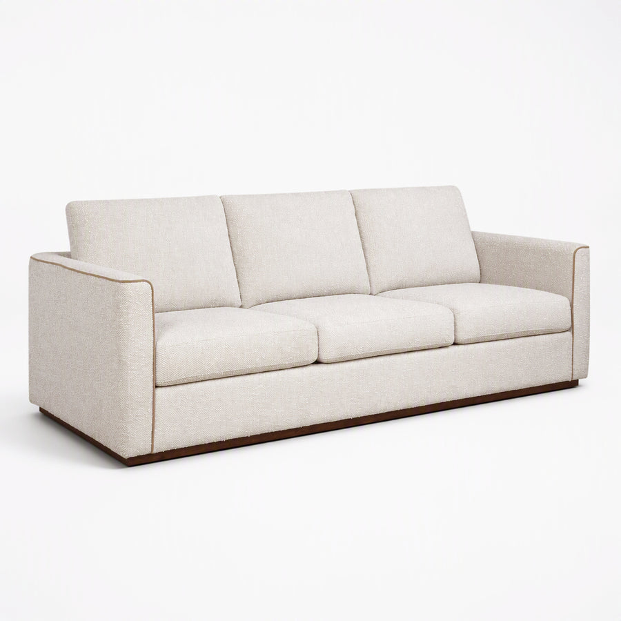 A modern three-seater sofa upholstered in a light beige textured fabric, featuring a low wooden base, shown on a seamless white background.