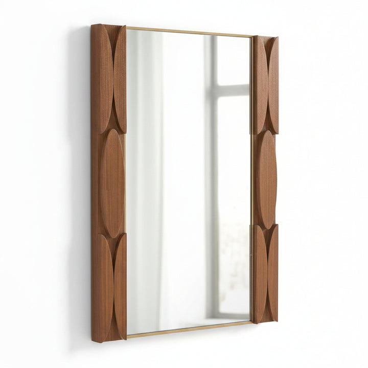 A rectangular wall mirror with a warm brown wood frame featuring sculpted, curved leaf-like panels on each side and a thin gold-toned metal trim.