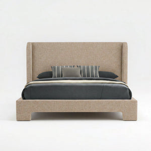 An upholstered bed frame with a tall wingback headboard and matching footboard, shown in a light beige fabric. The bed is styled with dark gray bedding, a striped gray pillow, and a solid gray accent pillow, set against a seamless white studio background.