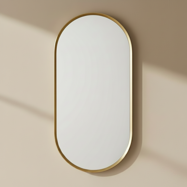 Oval mirror with gold frame on a beige wall