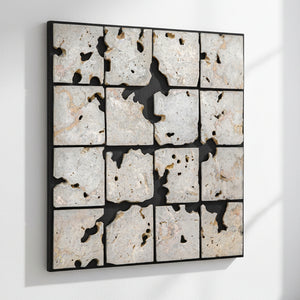 A square framed wall art piece composed of 16 irregular stone tiles arranged in a grid, separated by black grout or shadow lines. The stones are predominantly off-white, beige, and light gray with natural speckling and some darker voids showing through.