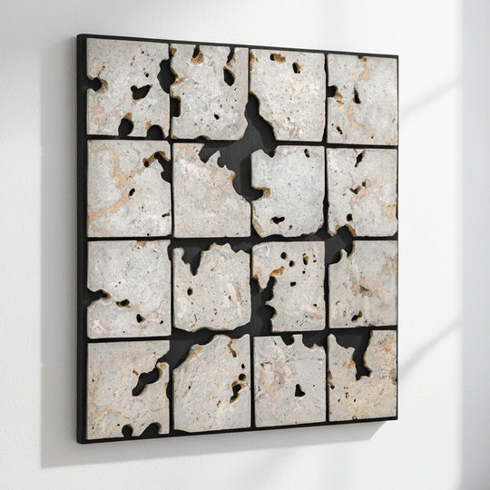 A square framed wall art piece composed of 16 irregular stone tiles arranged in a grid, separated by black grout or shadow lines. The stones are predominantly off-white, beige, and light gray with natural speckling and some darker voids showing through.