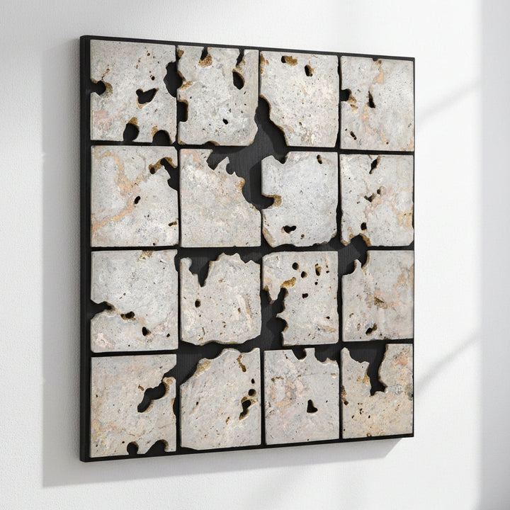 A square framed wall art piece composed of 16 irregular stone tiles arranged in a grid, separated by black grout or shadow lines. The stones are predominantly off-white, beige, and light gray with natural speckling and some darker voids showing through.