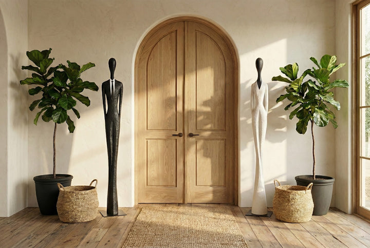 Wooden arched door with two mannequins and potted plants in a room with wooden flooring.