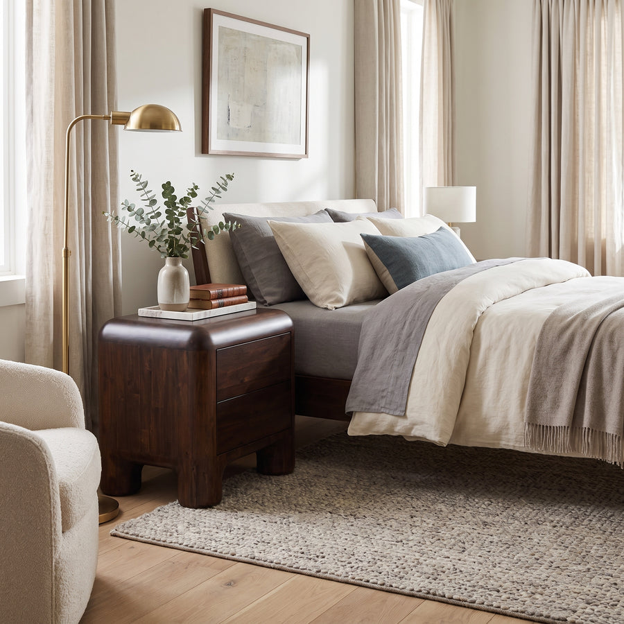 Rowan nightstand in a cozy bedroom setting, featuring a dark wood finish, rounded edges, and two storage drawers.