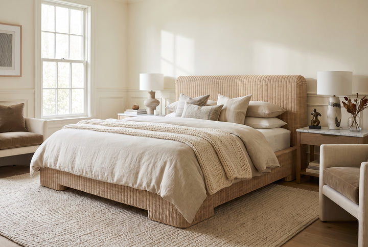 Modern coastal bedroom with a woven rattan bed, neutral linen bedding, and warm, minimalist decor.