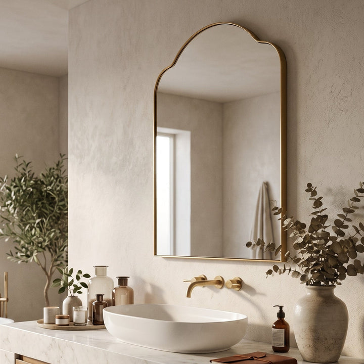 Sidney Arch Vanity Mirror in brass mounted above a marble and wood bathroom vanity in a bright, modern interior.