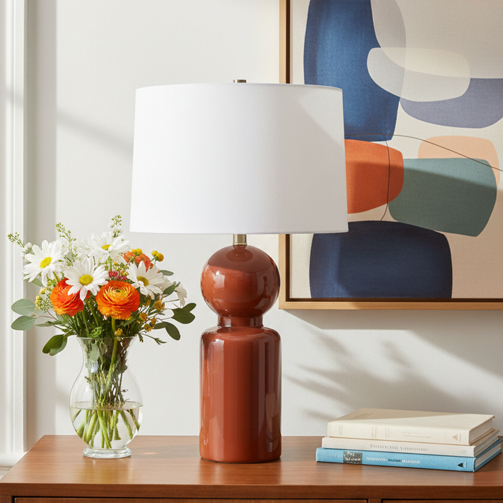 Decorative lamp with a vase of flowers and books on a table, with abstract art in the background.
