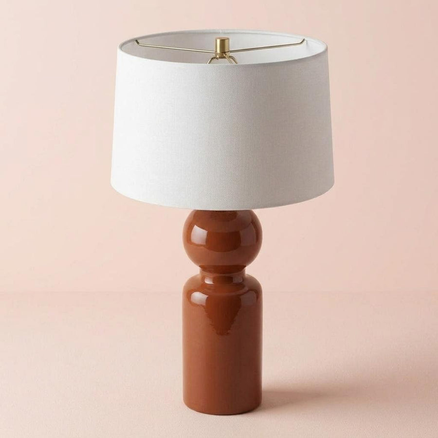 Table lamp with a brown base and white shade on a pink background