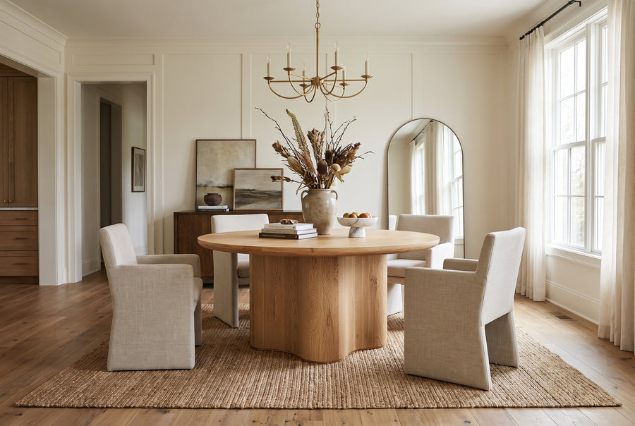Modern dining room with a round oak table, upholstered chairs, and neutral decor in a bright, minimalist home.