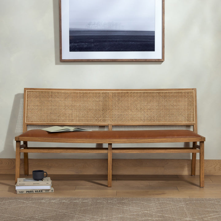 A stylish wooden bench with a cane backrest and brown leather cushion, adorned with a book and coffee mug on stacked books.