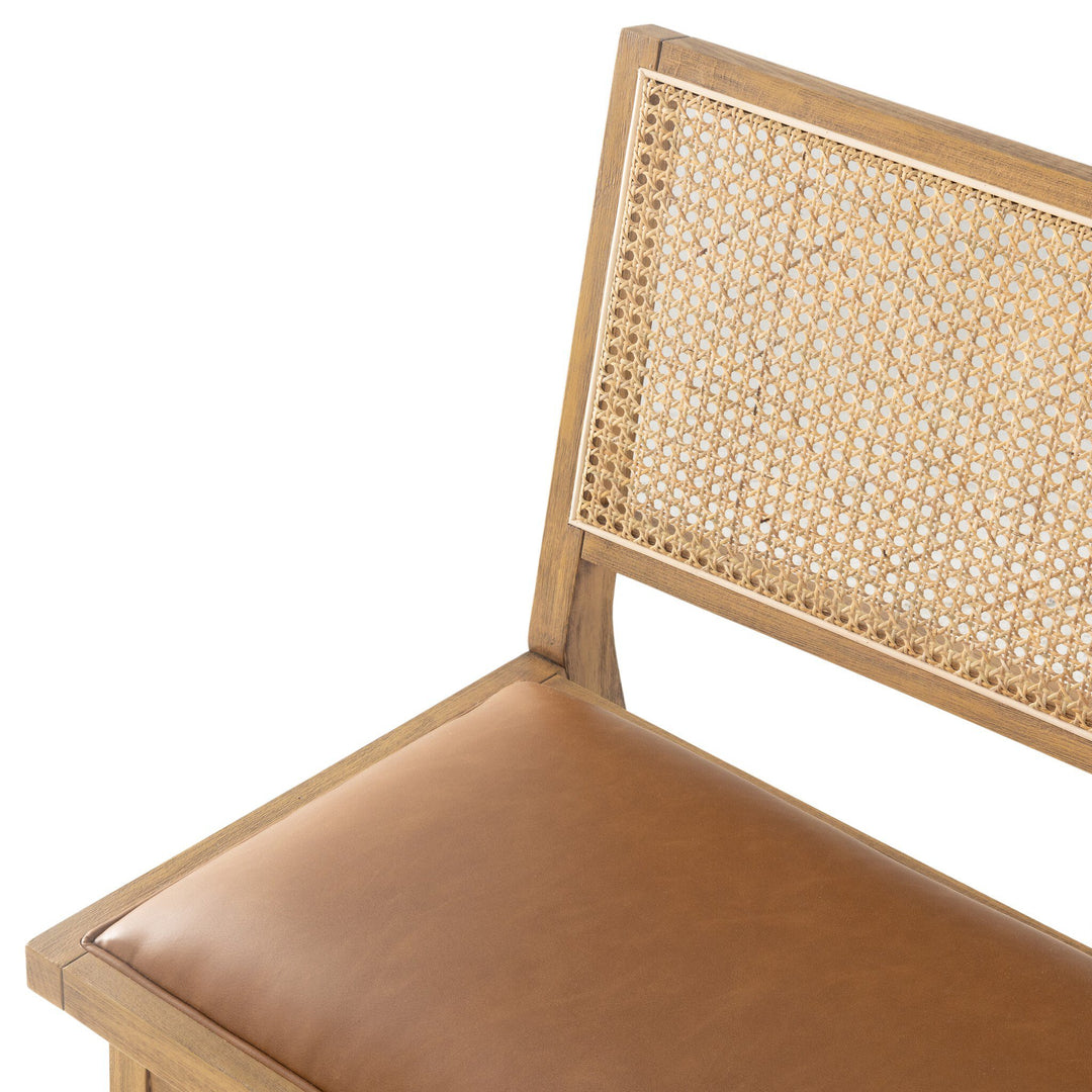 Close-up of a stylish bench featuring a cane backrest and a padded brown leather seat.