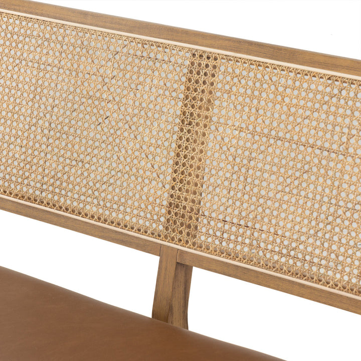 Close-up of a wooden bench's backrest, featuring woven cane texture and a sleek brown leather seat. 