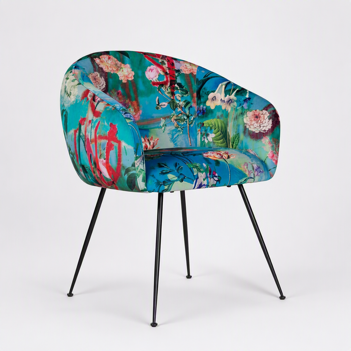 A modern accent chair with a vibrant, multicolored floral and botanical print upholstery on a white studio background. The chair features a rounded backrest and seat, supported by four thin black metal legs.