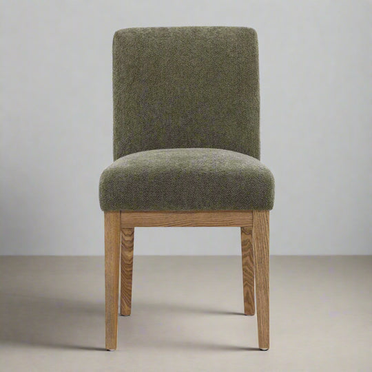 Green upholstered chair with wooden legs on a neutral background