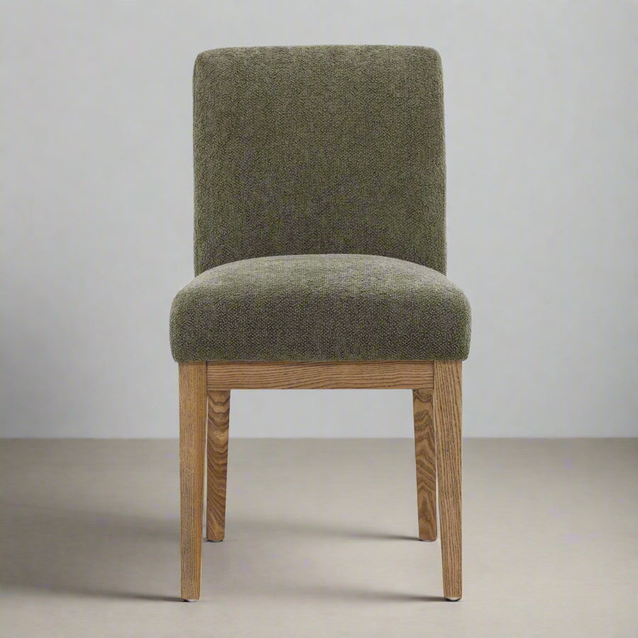 Green upholstered chair with wooden legs on a neutral background