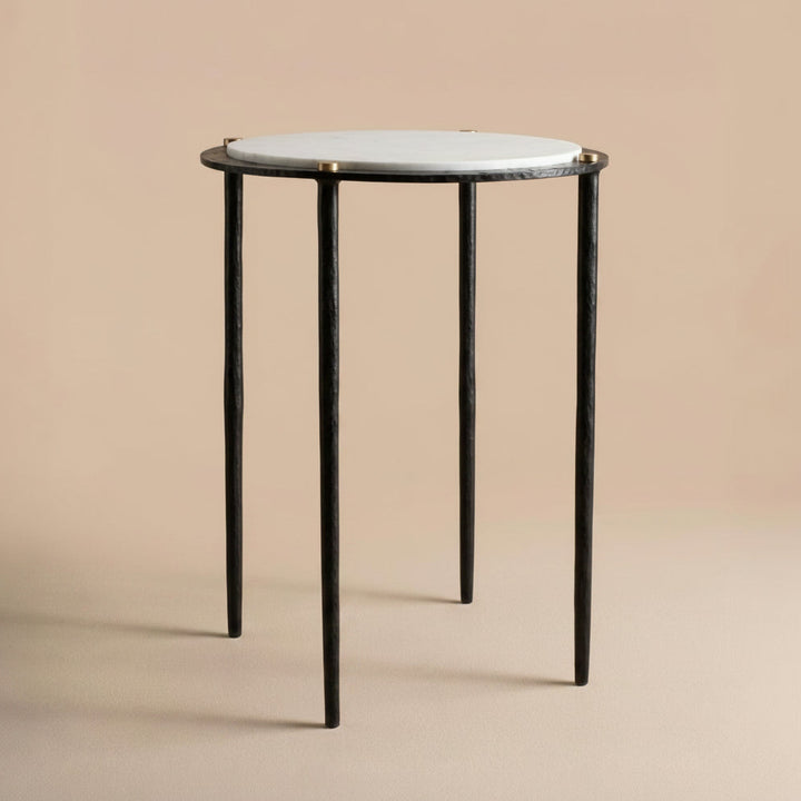 Small round table with a white marble top and dark bronze metal legs on a beige background