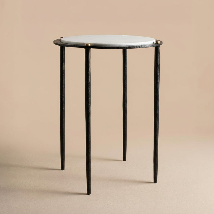 Small round table with a white marble top and dark bronze metal legs on a beige background