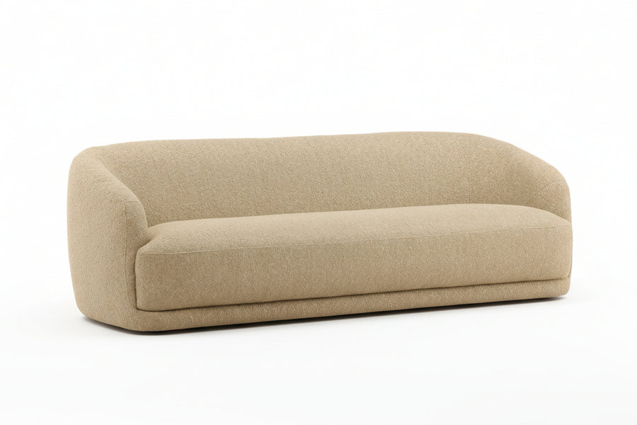 Beige upholstered sofa, rounded rectangular shape, textured fabric, low profile, minimalistic design, four short black legs, clean white background, modern furniture piece, soft edges, neutral tone