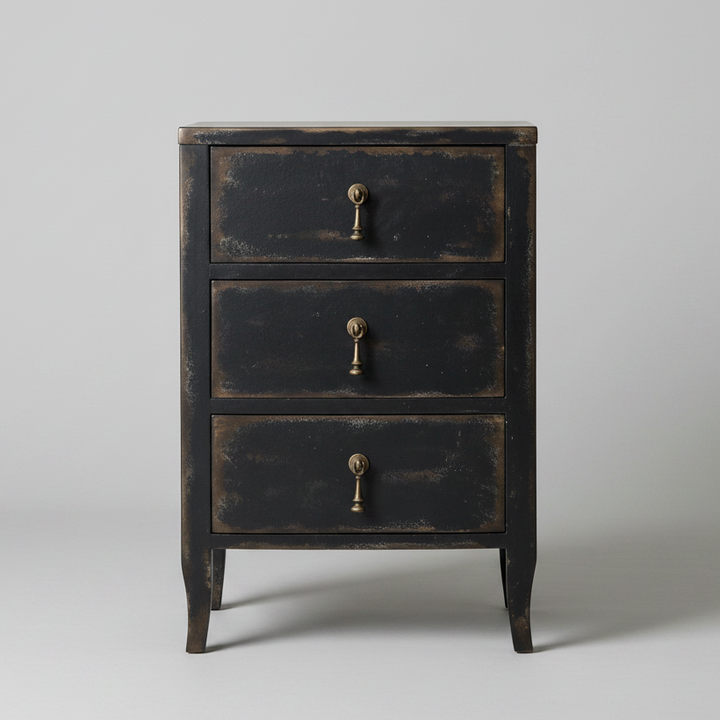 A three-drawer nightstand with a distressed black finish and antique brass drawer pulls, photographed against a neutral light gray background.