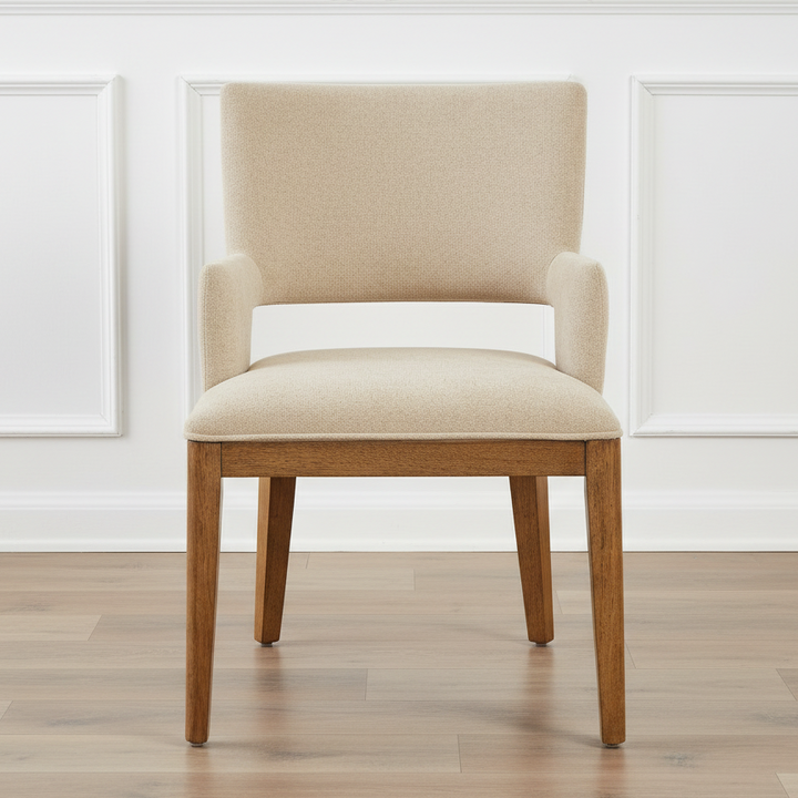 Beige upholstered chair with wooden legs on a wooden floor against a white paneled wall.