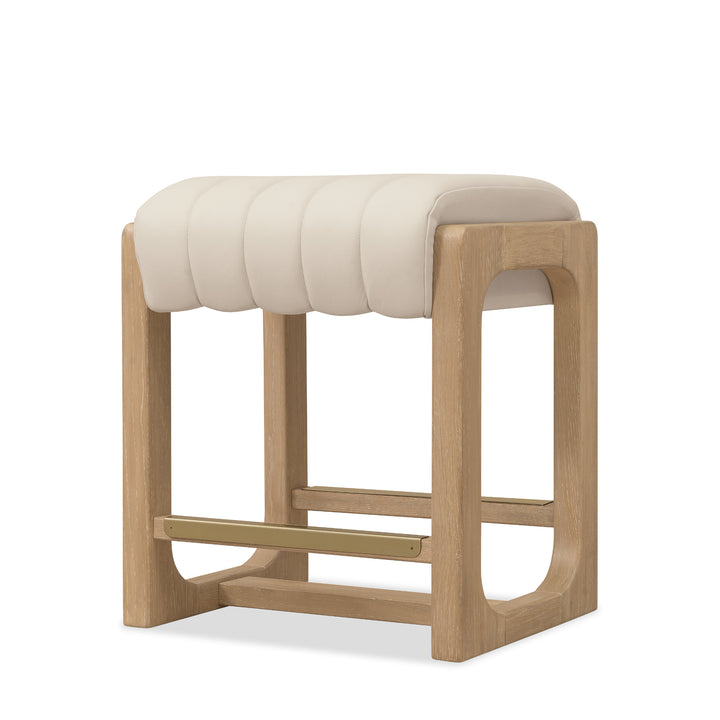 Angled view of a sunbleached beige leather counter stool with a padded, channel-tufted seat and a natural wood frame.