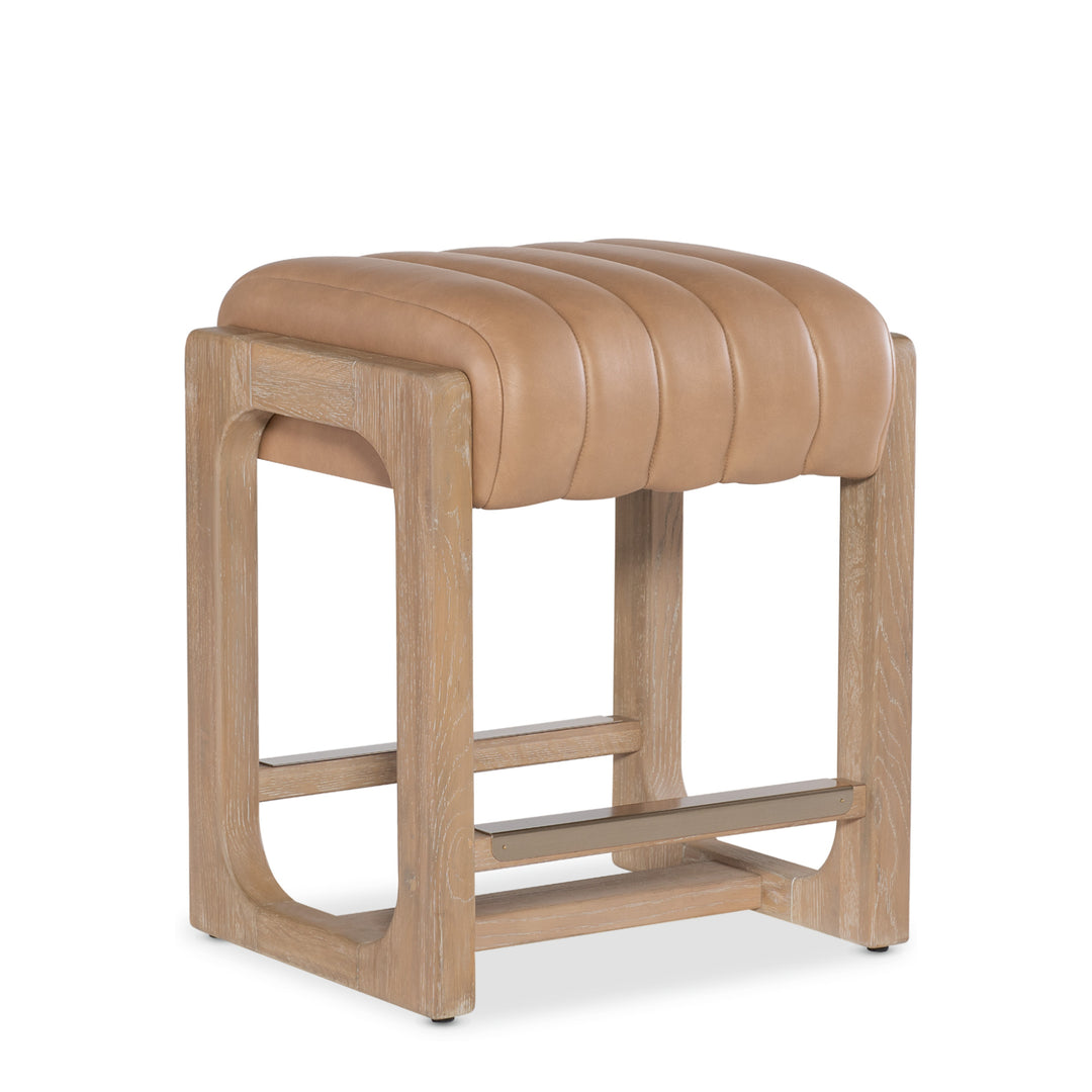 Angled view of a tan leather banyan counter stool wooden legs against a white background.