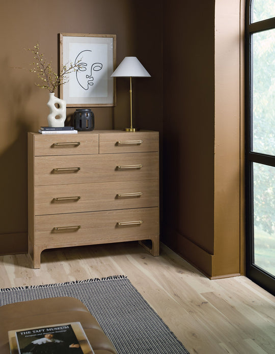 Wooden five-drawer dresser with a natural finish, set in a stylish bedroom.