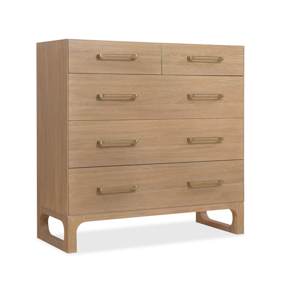 Angled view of a wooden dresser with a light oak finish, five drawers, and brass handles.