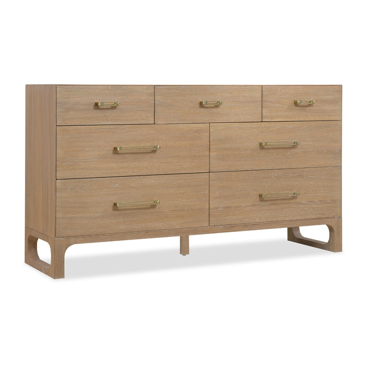 Wide wooden dresser with a light oak finish, seven drawers, brass handles, and open-cut wooden legs for support.