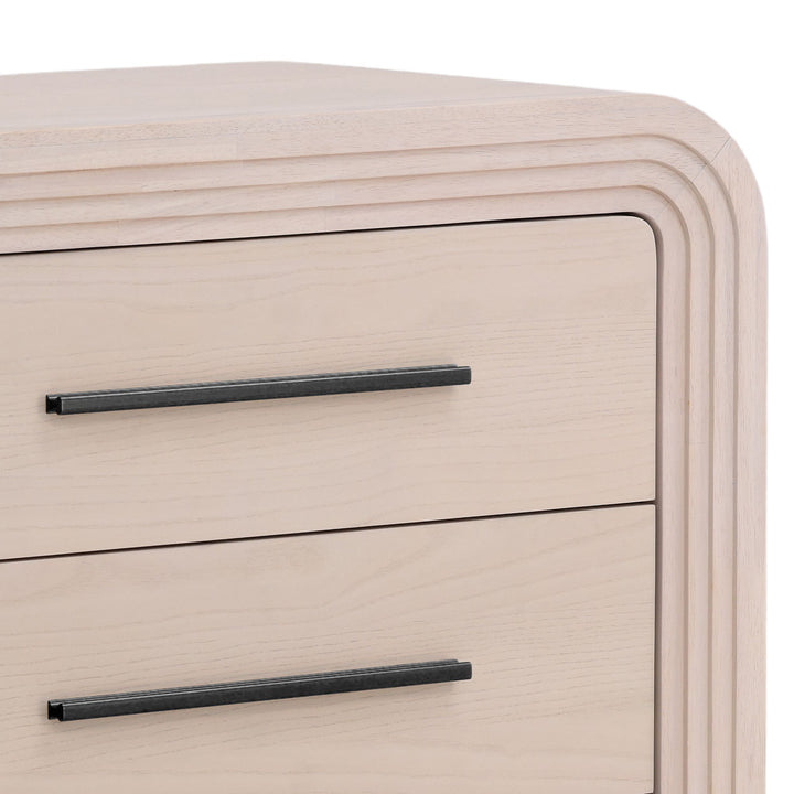 Close-up of a blanche wood dresser with six drawers, featuring sleek black handles and rounded edges.