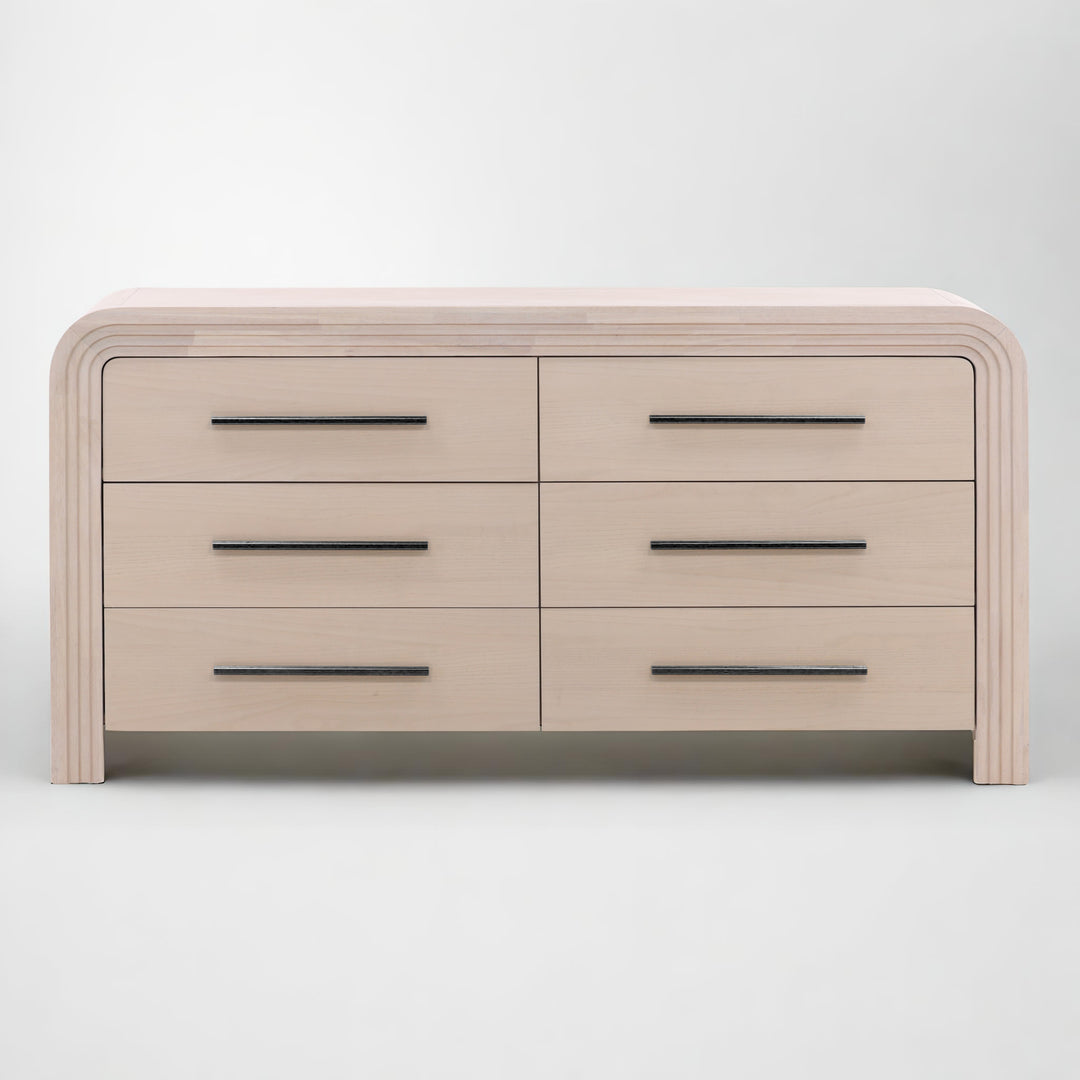 A modern light blanche wood dresser with six drawers, featuring sleek black handles and rounded edges.