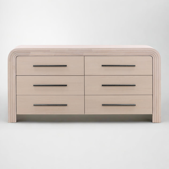 A modern light blanche wood dresser with six drawers, featuring sleek black handles and rounded edges.