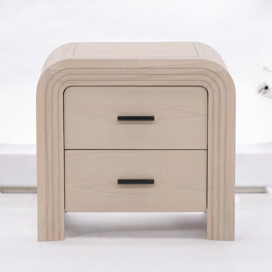 A modern light wood nightstand with a curved design featuring two drawers and sleek black handles.