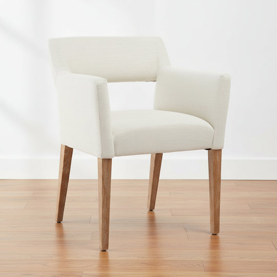 A white linen dining chair with a mid-open-back silhouette and oak wood legs, upholstered in a polyester blend fabric.