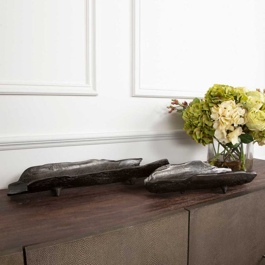 Two decorative wooden trays with a dark finish sit on a sleek wooden table.