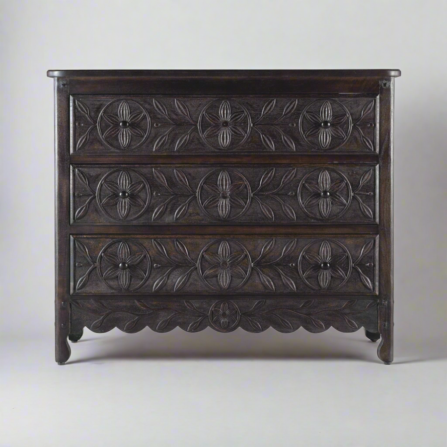 Dark wood dresser with intricate hand-carved floral and leaf patterns on three drawers, featuring a scalloped base and a traditional vintage design,.