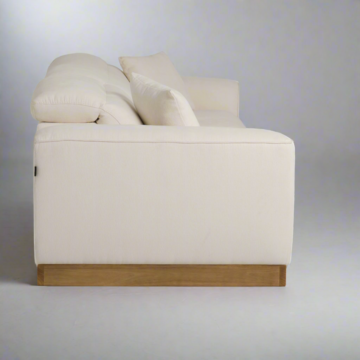 A modern white sofa with plush cushions and a wooden base, viewed from the side against a neutral gray background.