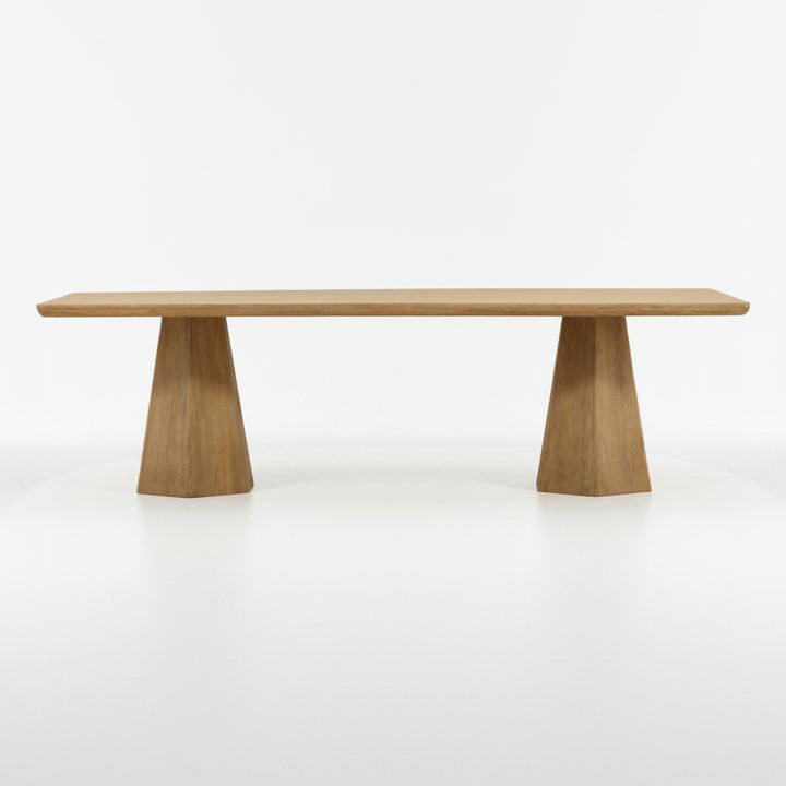 A modern wooden dining table with a rectangular light oak tabletop and two tapered geometric pedestal legs, shown against a plain white background.
