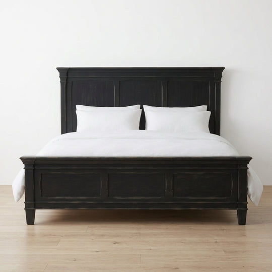 A black wooden bed frame with a tall panel headboard and matching footboard, shown dressed with white bedding and two white pillows