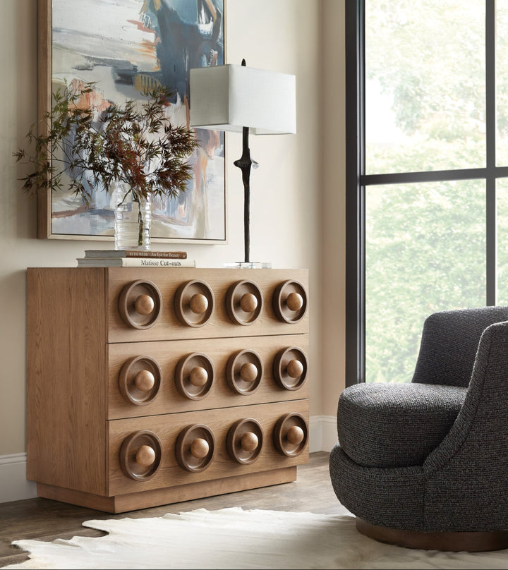 Wooden drawer chest with a geometric design featuring three rows of circular, recessed patterns and spherical knobs kept in decorated room.